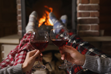 Couple with glasses of red wine near burning fireplace, closeup