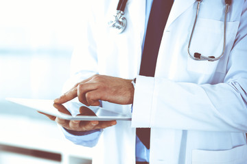 Obraz premium Doctor man using tablet computer for network research or virtual disease treatment, hands close-up. Perfect medical service in clinic. Modern medicine, medic data and healthcare concepts. Toned