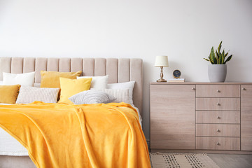 Stylish bedroom interior with soft yellow pillows and blanket