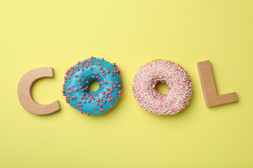 Word COOL made with wooden letters and donuts on yellow background, flat lay