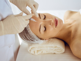 Obraz na płótnie Canvas Beautiful woman receiving beauty injections with closed eyes. Beautician doctor hands doing beauty procedure to female face with syringe. Cosmetic medicine and surgery concept