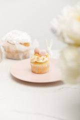 Selective focus of cupcake on plate and flowers on white background