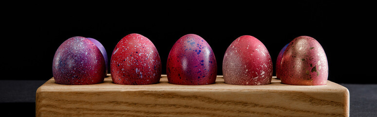 Colorful Easter eggs on wooden board on black background, panoramic shot