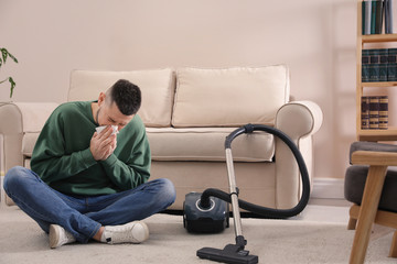 Man with vacuum cleaner suffering from dust allergy at home