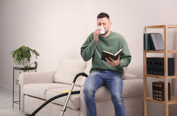 Man with book suffering from dust allergy at home