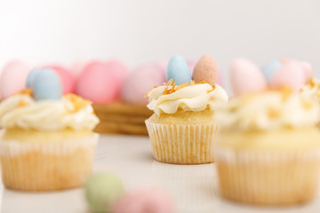 Selective focus of delicious cupcakes with easter eggs on wooden board on grey background