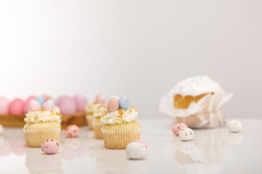 Selective focus of cupcakes with painted chicken and quail eggs near easter cake on grey background