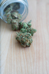 marijuana buds coming out of a jar on a light wood background