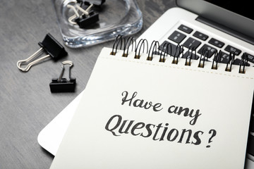 Notebook with phrase HAVE ANY QUESTIONS and laptop on grey table, closeup