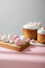 Easter eggs on wooden board with decorative rabbit with easter cakes on pink and grey