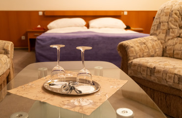 Hotel room`s interior with bad and two transparent wine glasses on the table