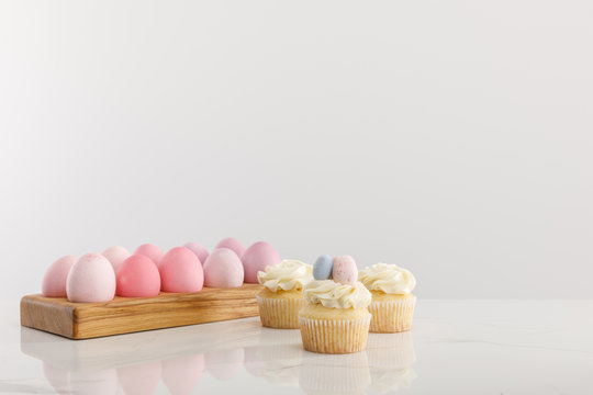 Easter eggs on egg tray with delicious cupcakes isolated on grey background