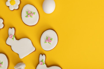 Top view of chicken egg, cookies and decorative bunny on yellow background