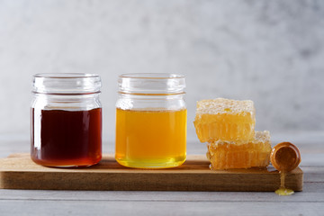Fresh honey and honeycombs on wooden cutting board. Light floral and dark honey in glass jars