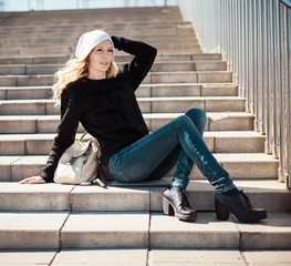 Fashion photo of a young beautiful woman in jeans, a black sweatshirt, a white knitted hat with a backpack