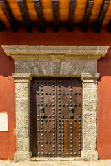 Old wooden door with stone jambs and cornice on a red wall in Cartagena city, Colombia.