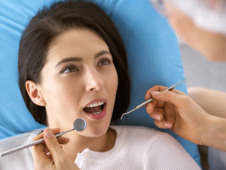 Smiling brunette woman being examined by dentist at dental clinic. Hands of a doctor holding dental instruments near patient's mouth. Healthy teeth and medicine concept