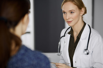 Cheerful smiling female doctor and patient woman discussing current health examination while...
