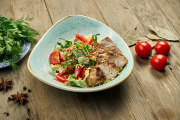 Warm salad with grilled turkey, tomatoes, pistachios, lettuce in a blue bowl on a wooden background. Healthy diet