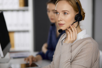 Businesswoman talking by headset while sitting in office. Call center and diverse people group in...