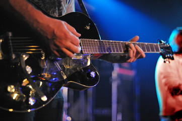 Close-up at musician playing guitar on stage illuminated by blue light.