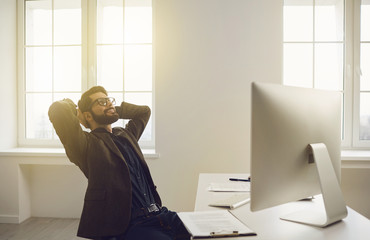 Businessman in glasses hands behind head contented dreams happy smiling sitting at a table in the...