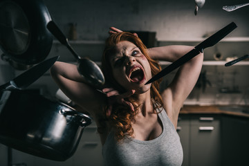 demoniacal yelling girl with levitating kitchenware in kitchen