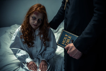 exorcist holding bible and hugging demoniacal girl in bedroom