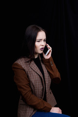 Joyful and successful young woman fashion blogger is emotionally talking on phone. Beautiful young woman in casual grey jacket is holding smartphone