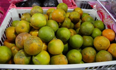 Plastic tray of green and yellow citrus fruits at a fruit stall