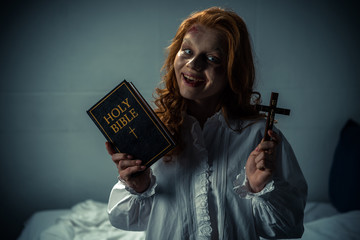 smiling demoniacal woman holding cross and holy bible