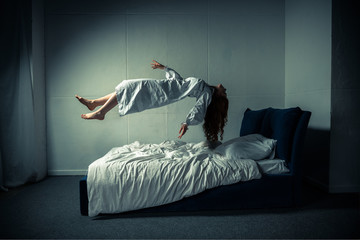 creepy woman in nightgown sleeping and levitating over bed - obrazy, fototapety, plakaty