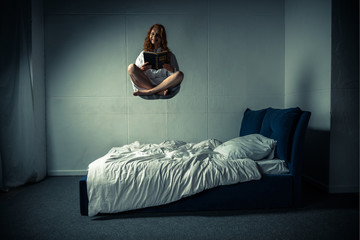 creepy smiling girl in nightgown levitating over bed while reading bible