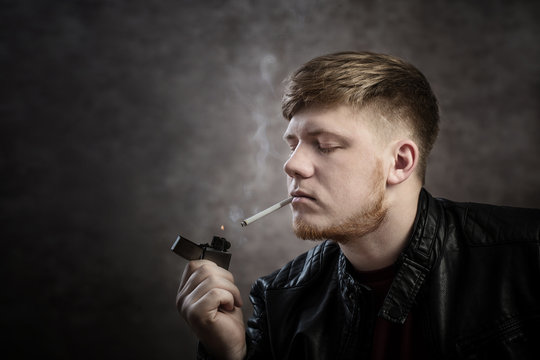 Young man in  leather jacket smokes cigarette on dark background