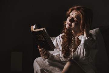 creepy demoniacal crying woman reading holy bible on bed