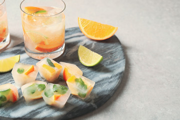 Ice cubes with orange and mint on light grey table