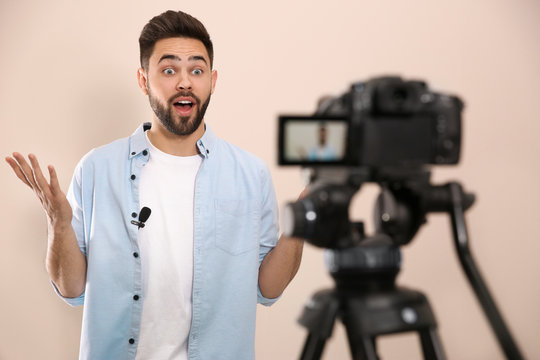 Young blogger recording video on camera against beige background