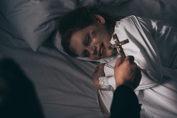 exorcist holding cross over demonic obsessed smiling girl in bed