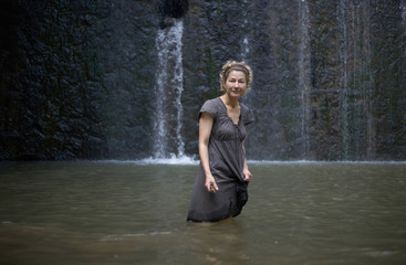 Relaxed smiling woman enjoying summer standing in the water of a rocky waterfall
