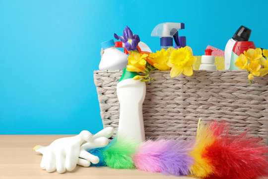Wicker basket with spring flowers and cleaning supplies on wooden table