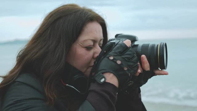 Woman wearing gloves with camera takes pictures on the beach
