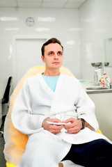 Beauty esthetics treatment. Waist up portrait of young brunette male in white bathrobe lying on couch ready for cosmetology procedure cosmetic center