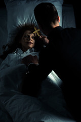 Exorcist holding cross over female creepy demon in bed