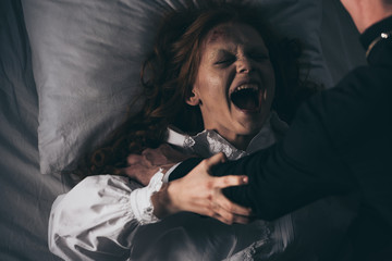 exorcist holding yelling female demon in bed