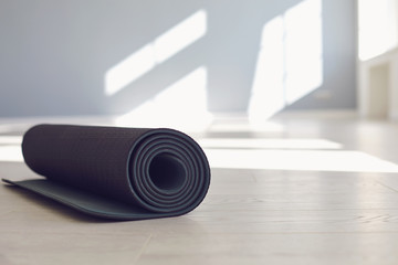 Black yoga mat on the floor of a bright sunny studio.