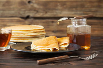 puncakes with honey and cup of tea on old wooden background