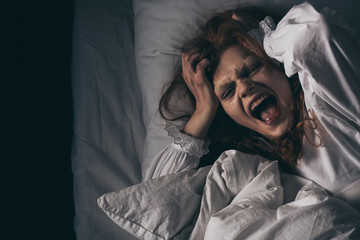 top view of obsessed girl in nightgown screaming while lying in bed