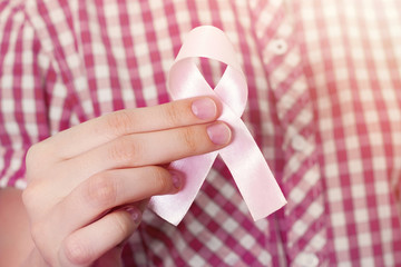 A girl in a checked shirt holds a pink breast cancer awareness ribbon. Concept of medicine, health...