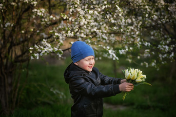 Portrait of a boy with a bouquet of tulips on a background of flowering trees