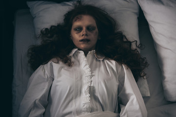 top view of obsessed creepy girl in nightgown lying in bed